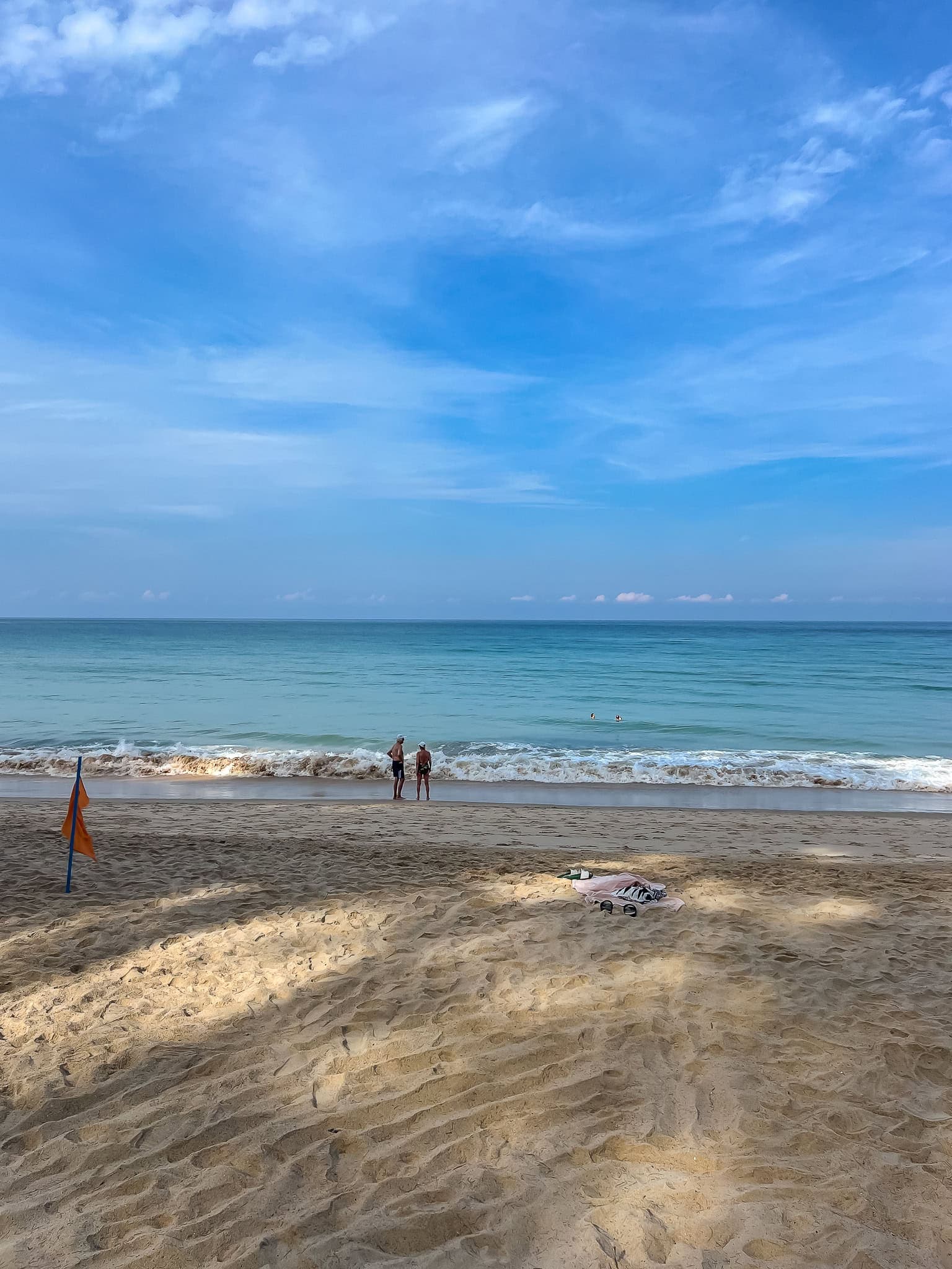 an orange warning flag on the sand with waves behind it